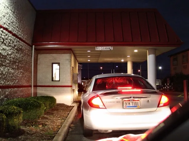 Autó várakozik a gyorséttermi drive-thru ablaknál esti kiszolgáláson